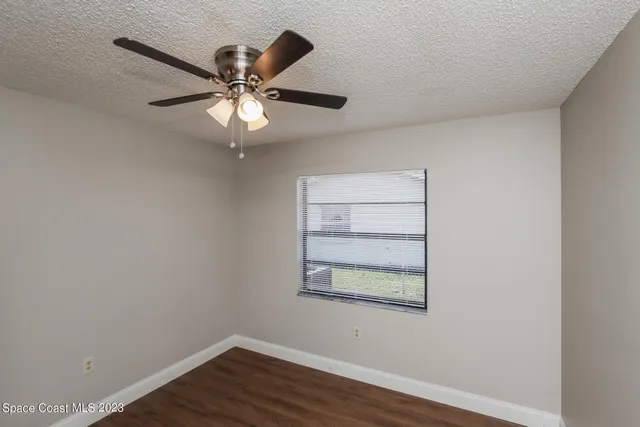 an empty room with wooden floor chandelier fan and windows