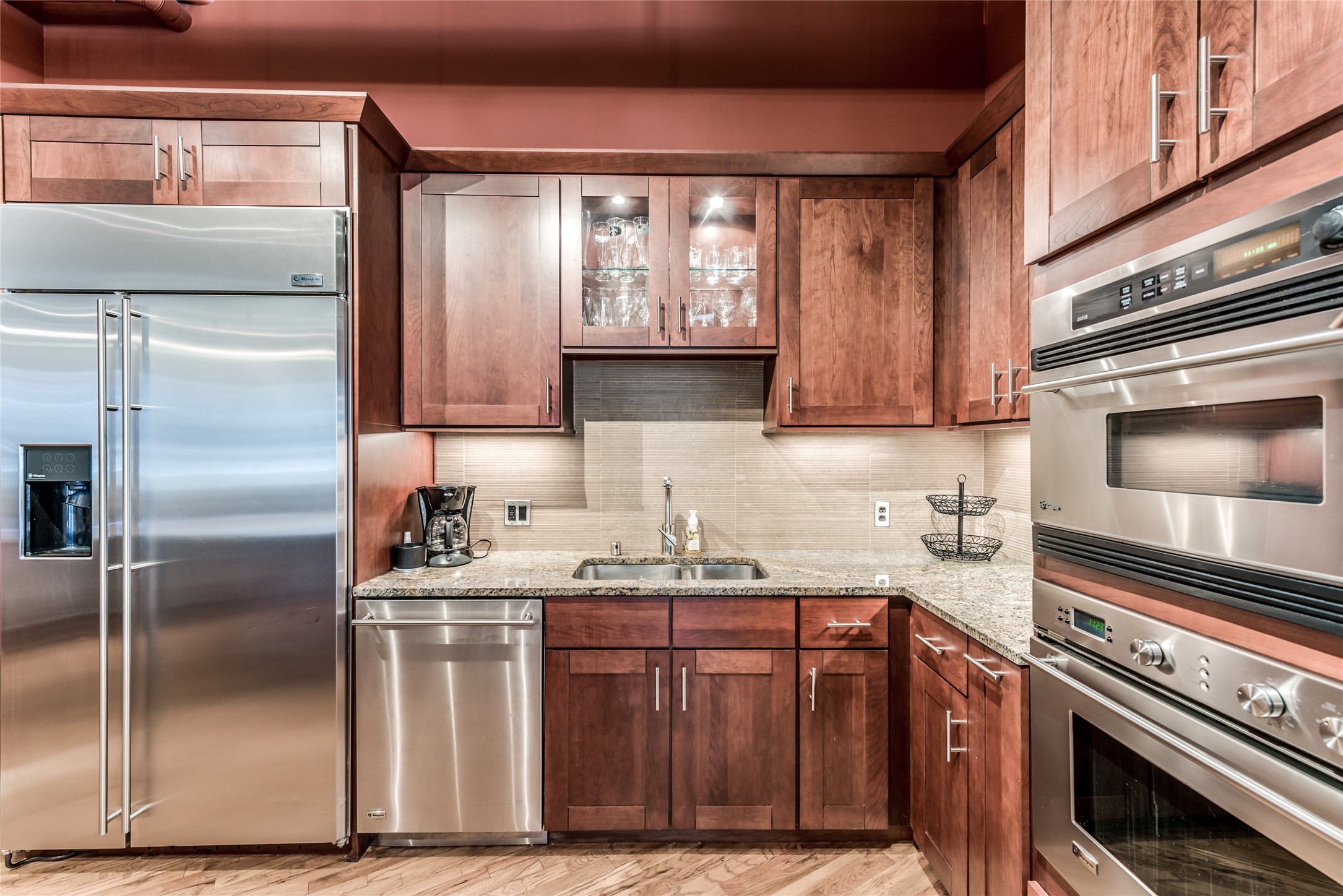 705 Main Street, Unit 215 Houston, TX 77002 - Photo 5 of 36 This kitchen features modern stainless steel appliances, including a double oven and a large fridge. It has rich wooden cabinetry, granite countertops, and a stylish tile backsplash, offering both functionality and elegance.