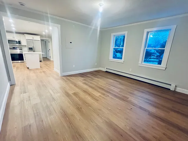 a view of empty room with wooden floor and kitchen view