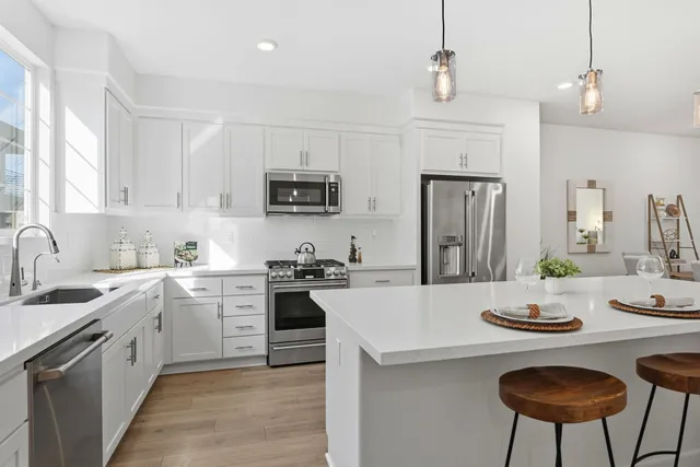 a large white kitchen with a refrigerator a stove a sink a dining table and chairs