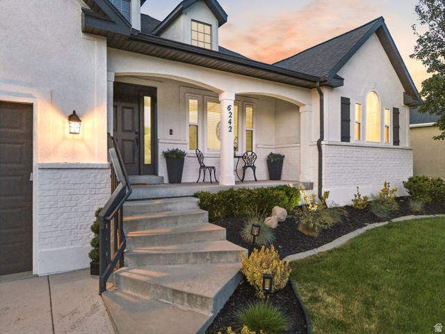 6242 Apollo Way Highland, UT 84003 - Photo 3 of 47 White stucco and brick exterior featuring a covered porch with white columns, concrete steps, and a dark entry door