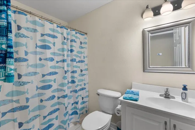 a bathroom with a granite countertop toilet a sink a mirror and shower curtain