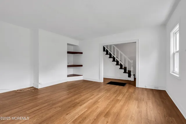a view of an empty room with wooden floor and stairs