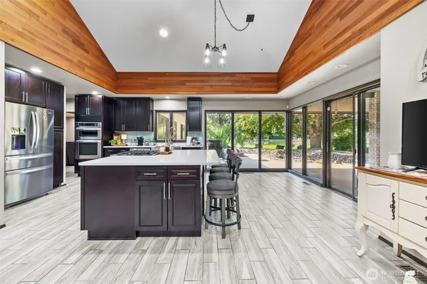 a kitchen with stainless steel appliances granite countertop a refrigerator a sink dishwasher a stove and a dining table with wooden floor