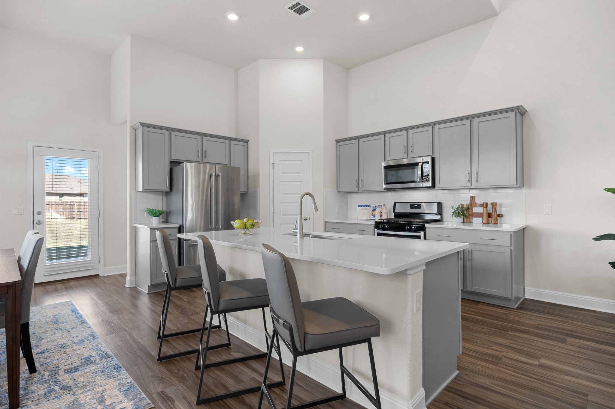16804 Guido Cove Pflugerville, TX 78660 - Photo 6 of 38 Kitchen with gray cabinetry, a towering ceiling, stainless steel appliances, dark wood-type flooring, and a center island with sink