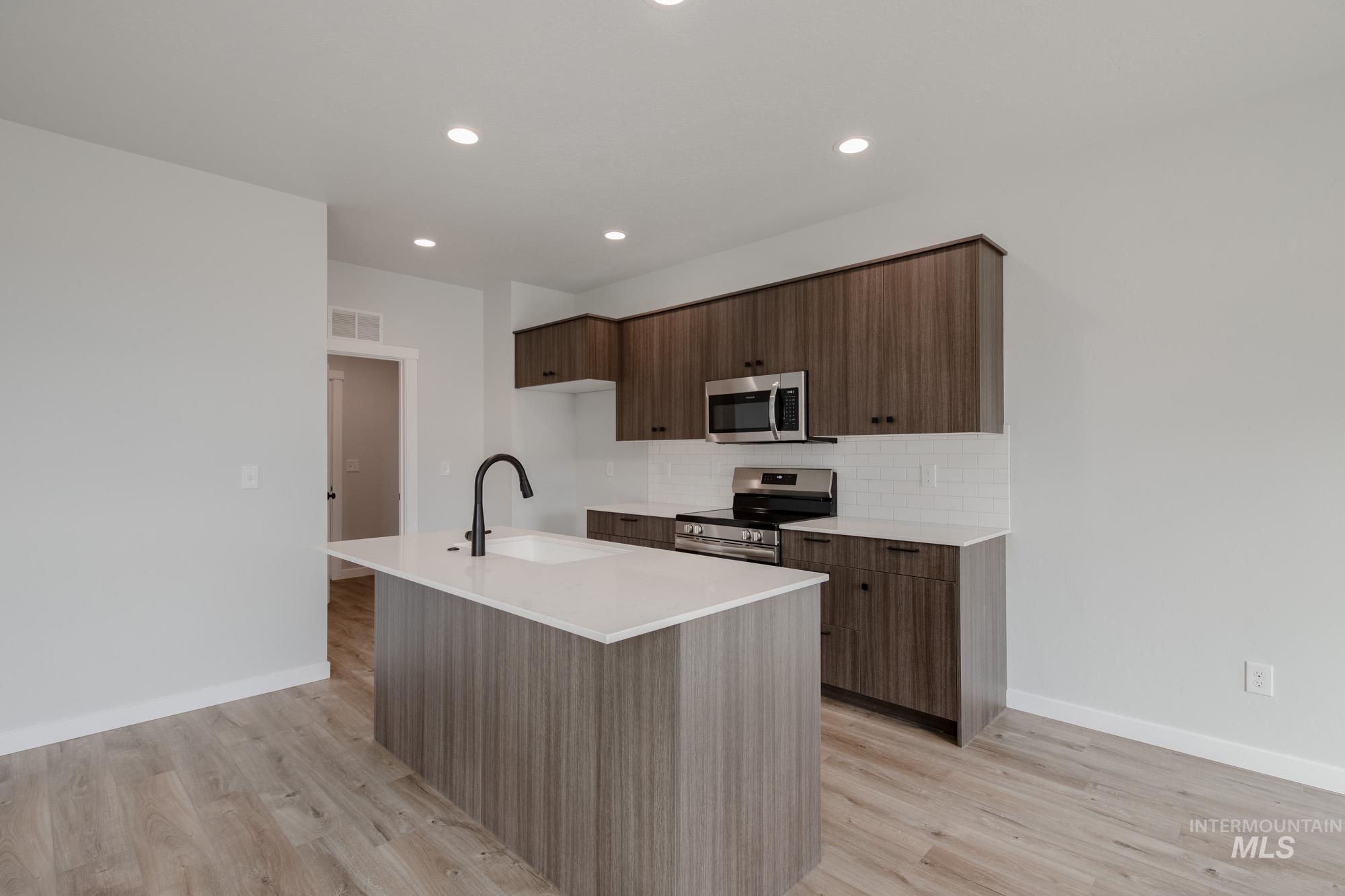 2192 South Border Way Meridian, ID 83642 - Photo 3 of 22 Kitchen with modern cabinets, a kitchen island with sink, stainless steel appliances, light wood-style flooring, and light stone counters