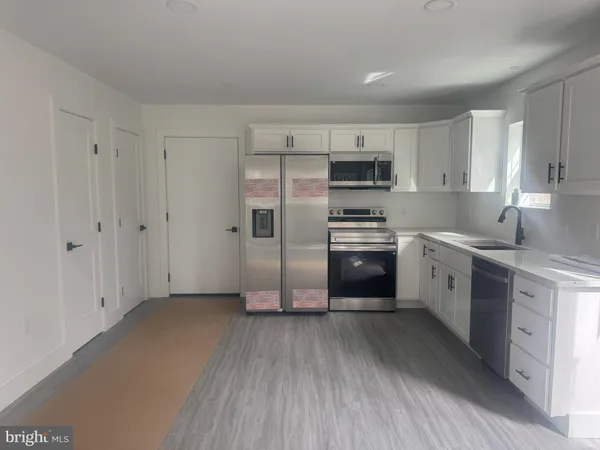 a kitchen with stainless steel appliances a stove a sink dishwasher a refrigerator with white cabinets and wooden floor