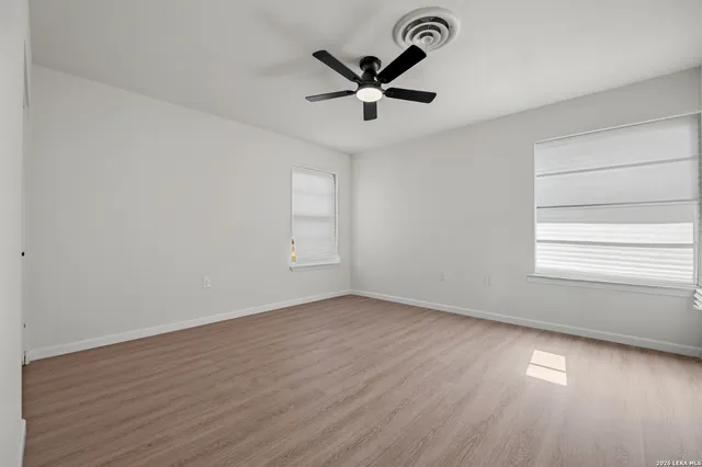 an empty room with wooden floor ceiling fan and windows