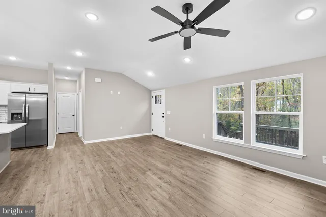 an empty room with wooden floor a ceiling fan and windows