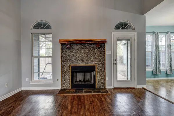 a view of an empty room with wooden floor fireplace and a window