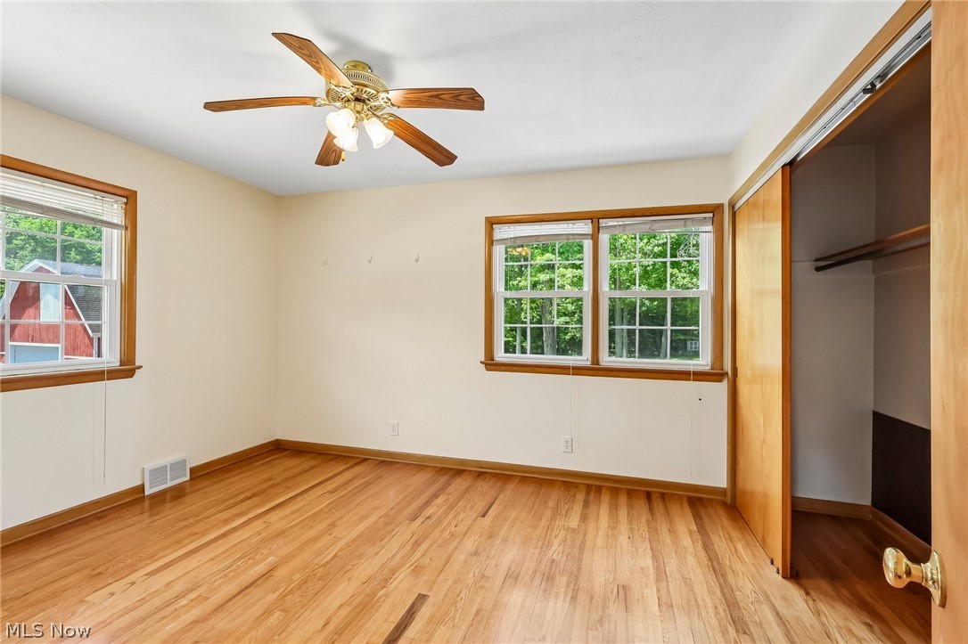 1638 South Cleveland Massillon Road Akron, OH 44321 - Photo 13 of 37 Spacious room featuring hardwood flooring, a ceiling fan with light fixture, multiple windows with natural wood trim, and a built-in closet with sliding wood doors