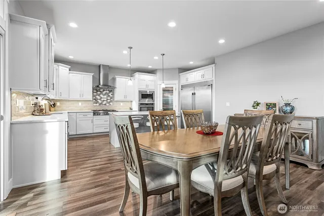 a kitchen with stainless steel appliances kitchen island granite countertop a dining table chairs and white cabinets