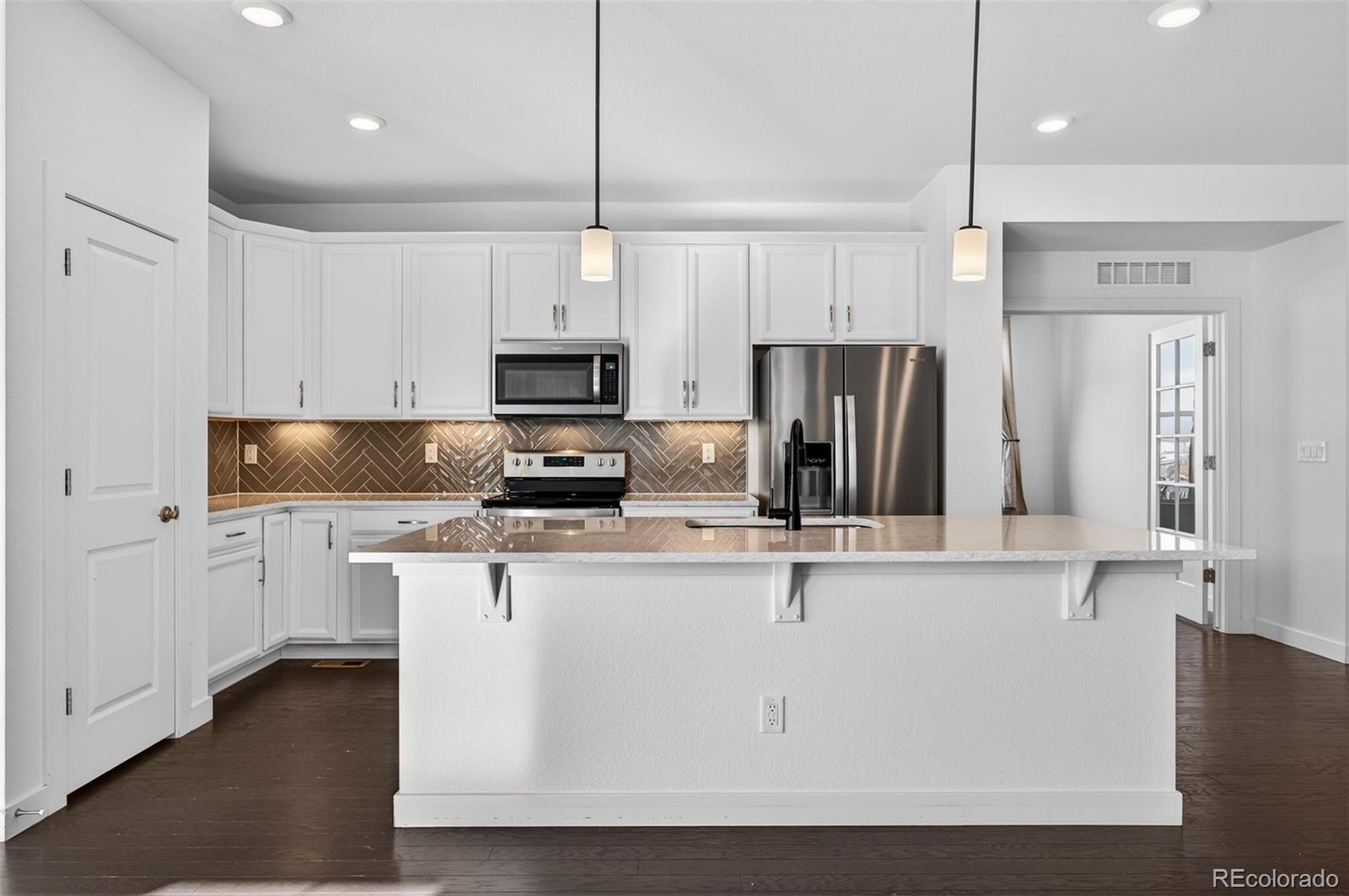 6311 Stable View Street Castle Pines, CO 80108 - Photo 9 of 46 a kitchen with stainless steel appliances granite countertop a refrigerator a stove a sink and white cabinets with wooden floor