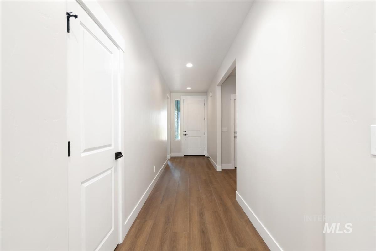 Bright hallway featuring wood-finish flooring, recessed lighting, white trim, and white paneled doors with matte black hardware