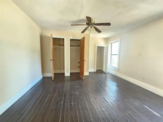 an empty room with wooden floor a ceiling fan and windows