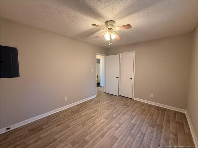 a view of an empty room with wooden floor and a ceiling fan