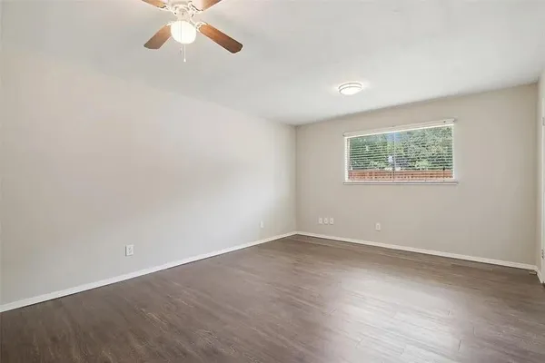 an empty room with wooden floor chandelier fan and windows