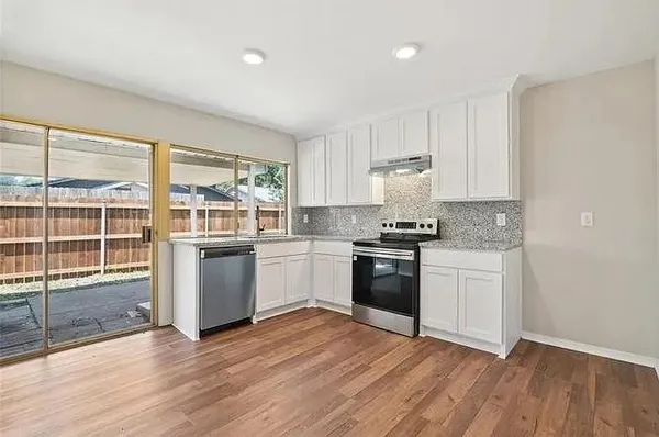 a kitchen with granite countertop a stove a sink and white cabinets with wooden floor