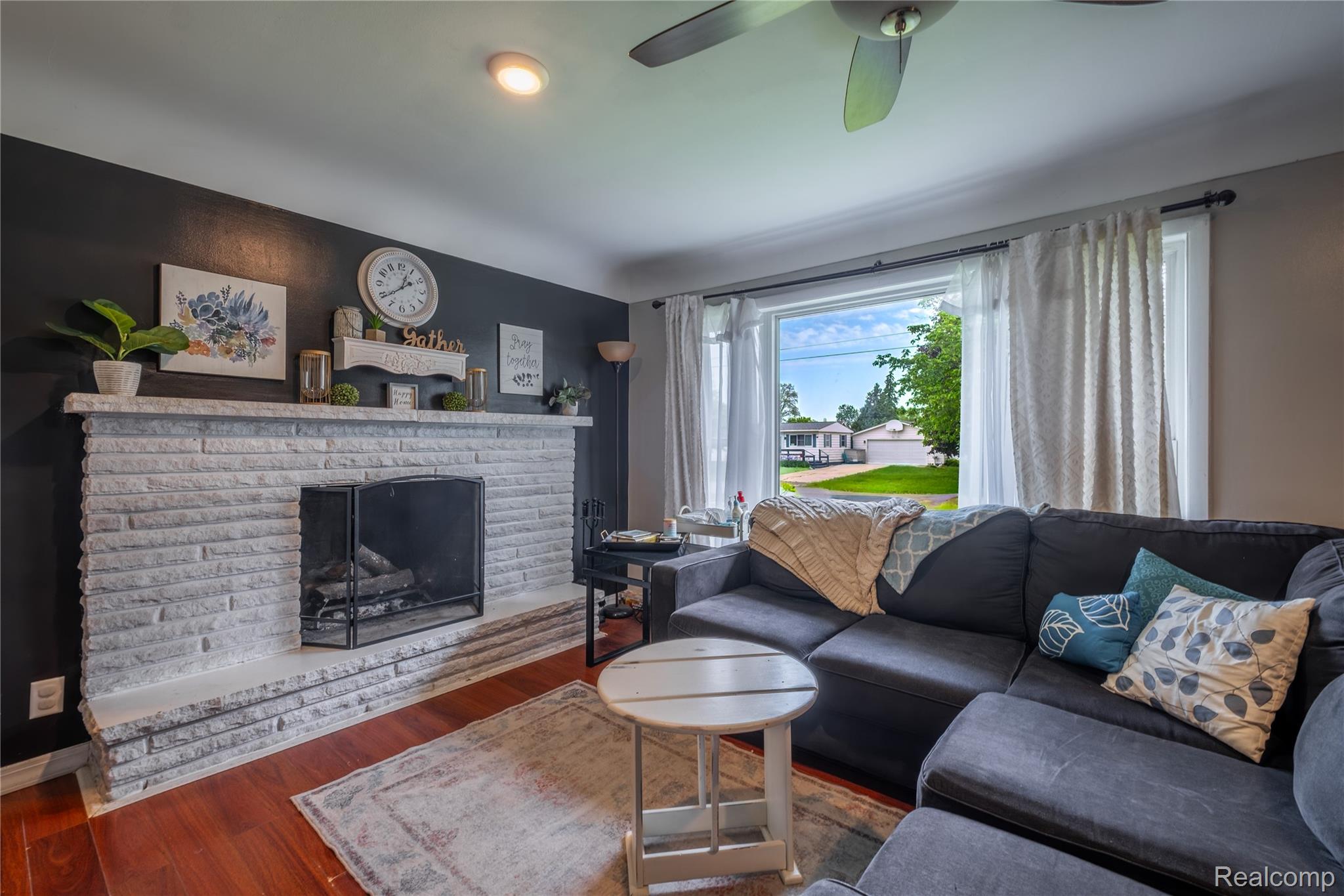7800 Maple Street Birch Run, MI 48415 - Photo 3 of 29 Living area featuring a stone-clad fireplace with a black metal screen, rich wood-finish flooring, and a ceiling fan