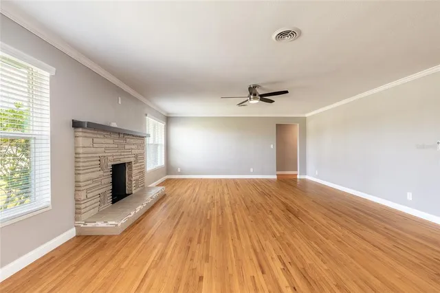 an empty room with wooden floor fireplace and windows