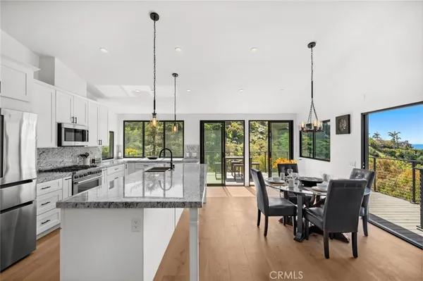 a kitchen with stainless steel appliances granite countertop a stove top oven a sink a dining table and chairs with wooden floor