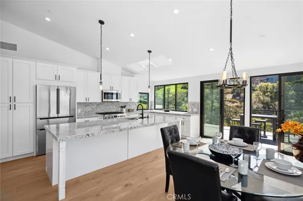 a kitchen with stainless steel appliances kitchen island granite countertop a stove a refrigerator a sink a dining table and chairs with wooden floor