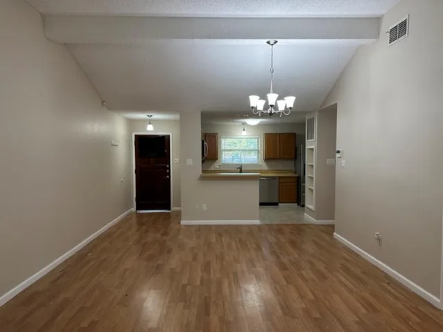 an empty room with wooden floor and kitchen view