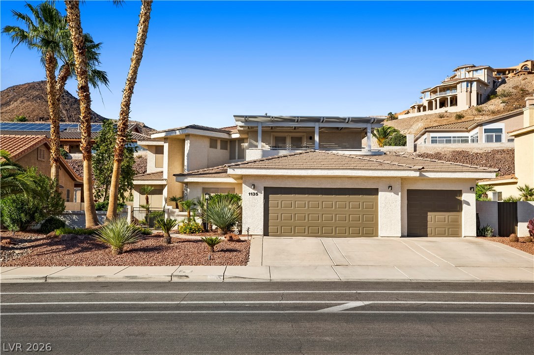 1135 Calico Ridge Drive Henderson, NV 89011 - Photo 2 of 86 A spacious home with desert landscaping and an inviting attached garage, poised against a clear blue sky.