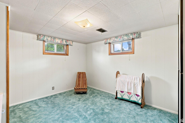 702 North 150 West Logan, UT 84321 - Photo 29 of 51 Carpeted room with white paneled walls, two windows with wood trim, and a drop ceiling with a central light fixture