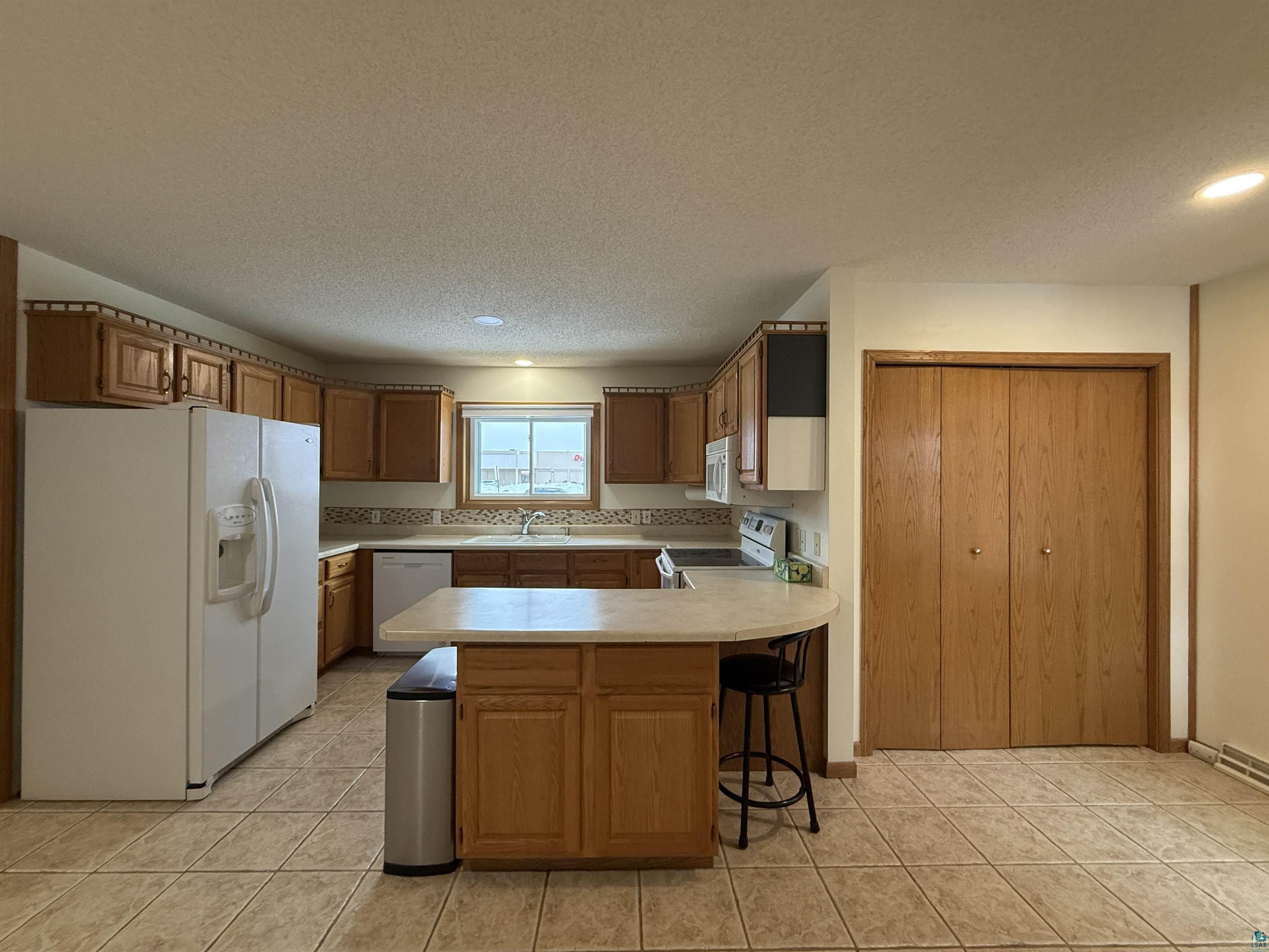 1321 South 13th Street Virginia, MN 55792 - Photo 4 of 33 Kitchen with a peninsula, white appliances, light countertops, wood finish cabinets, and a textured ceiling