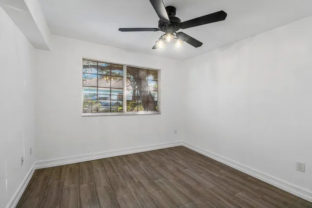 an empty room with wooden floor fan and windows