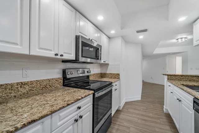 a kitchen with granite countertop a sink stainless steel appliances and white cabinets