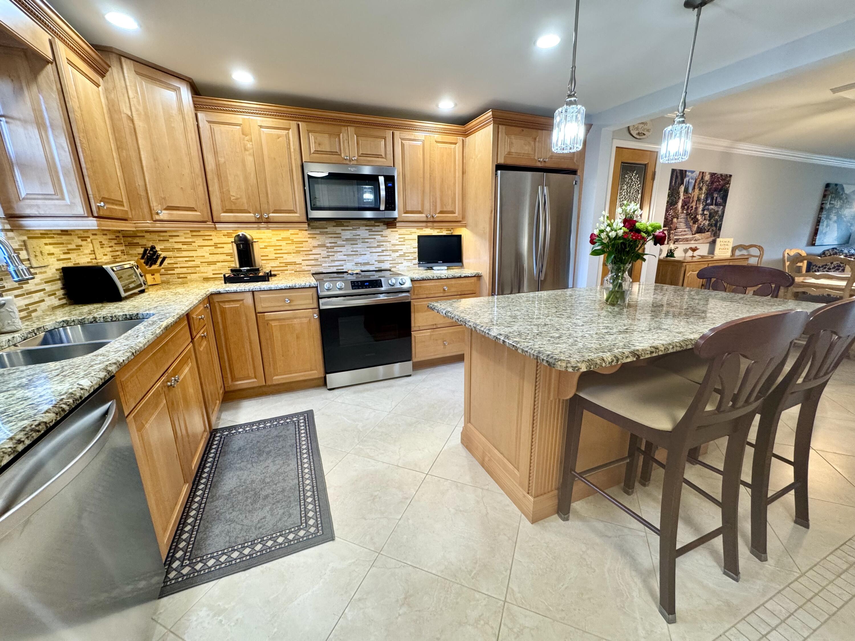 300 North Hwy A1A, Unit 104O Jupiter, FL 33477 - Photo 6 of 25 a kitchen with stainless steel appliances granite countertop a table chairs sink refrigerator and microwave
