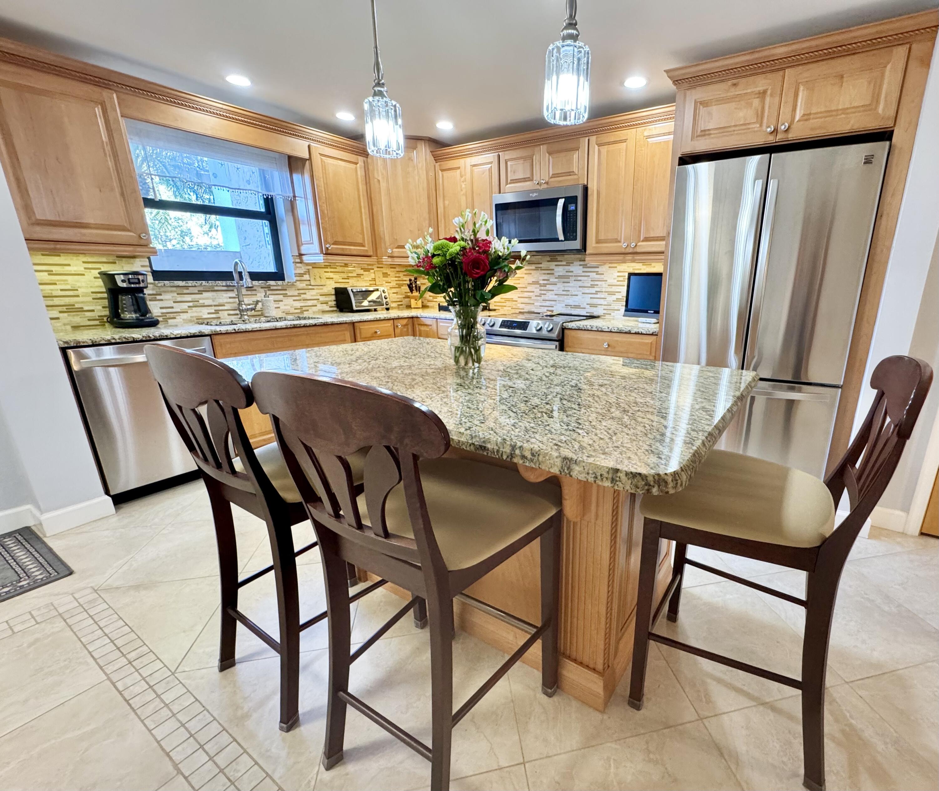 300 North Hwy A1A, Unit 104O Jupiter, FL 33477 - Photo 7 of 25 a kitchen with stainless steel appliances granite countertop table chairs sink refrigerator and microwave