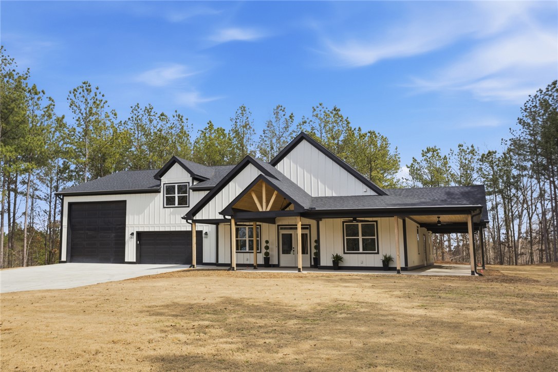 This modern farmhouse features charming porches and a spacious attached garage, set against a backdrop of mature trees.