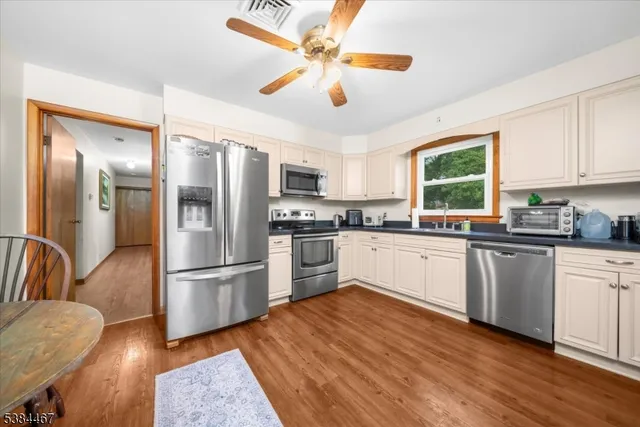 a kitchen with granite countertop a refrigerator oven a sink dishwasher and white cabinets with wooden floor