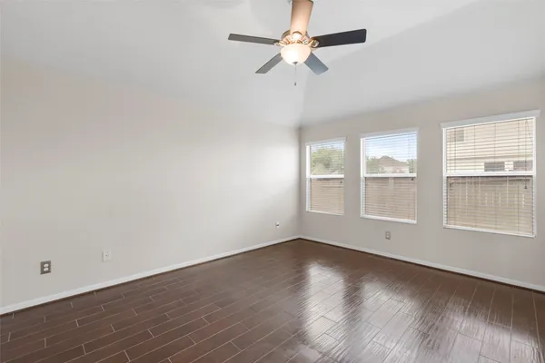 an empty room with wooden floor fan and windows