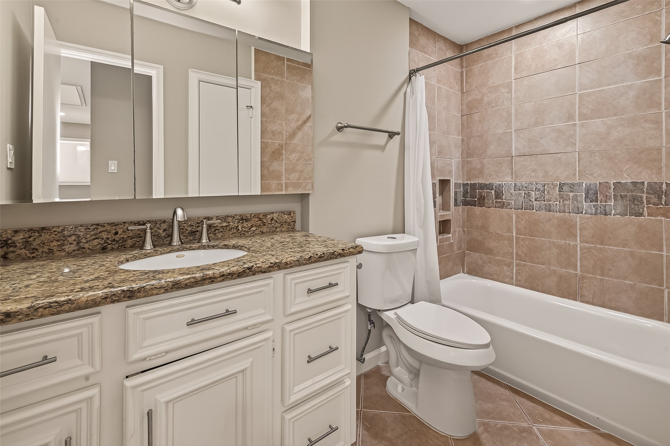 10810 Umber Court Houston, TX 77099 - Photo 22 of 43 The secondary bathroom is a stylish retreat featuring a spacious vanity with a granite countertop and plenty of cabinet storage. The shower-tub combination is beautifully finished with floor-to-ceiling tile work and a decorative mosaic inlay, adding a high-end feel for guests or family members.