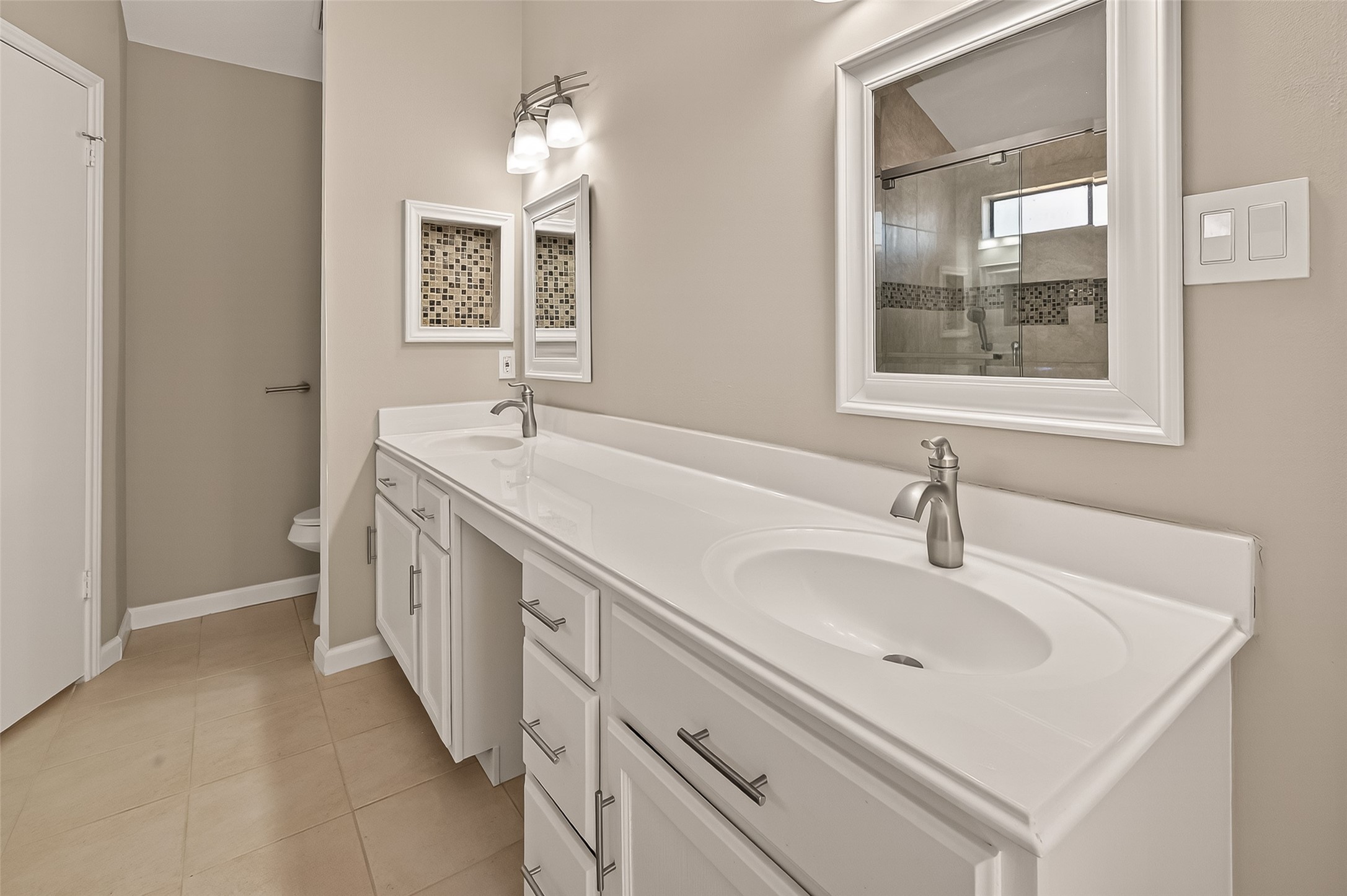 10810 Umber Court Houston, TX 77099 - Photo 28 of 43 Efficiency meets style in the primary ensuite, featuring a long vanity with ample cabinet storage and modern fixtures. The layout provides plenty of room for morning routines while maintaining a sleek, uncluttered look.