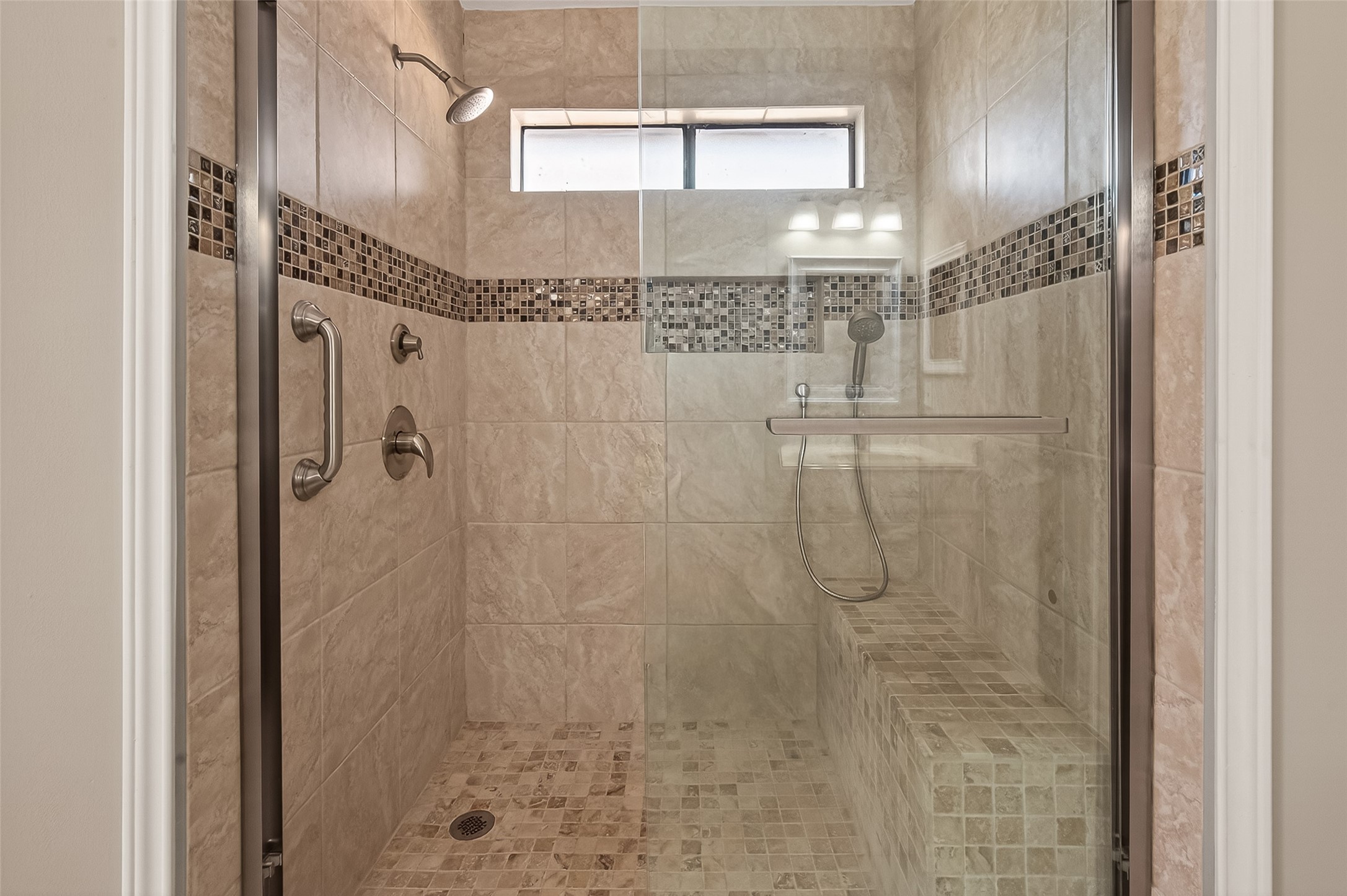 10810 Umber Court Houston, TX 77099 - Photo 30 of 43 The primary bathroom’s shower is designed for both style and relaxation, featuring beautiful floor-to-ceiling tile work. A decorative mosaic tile inlay adds a sophisticated, custom touch, while the updated fixtures and clean, neutral grout give the space a fresh, modern feel.