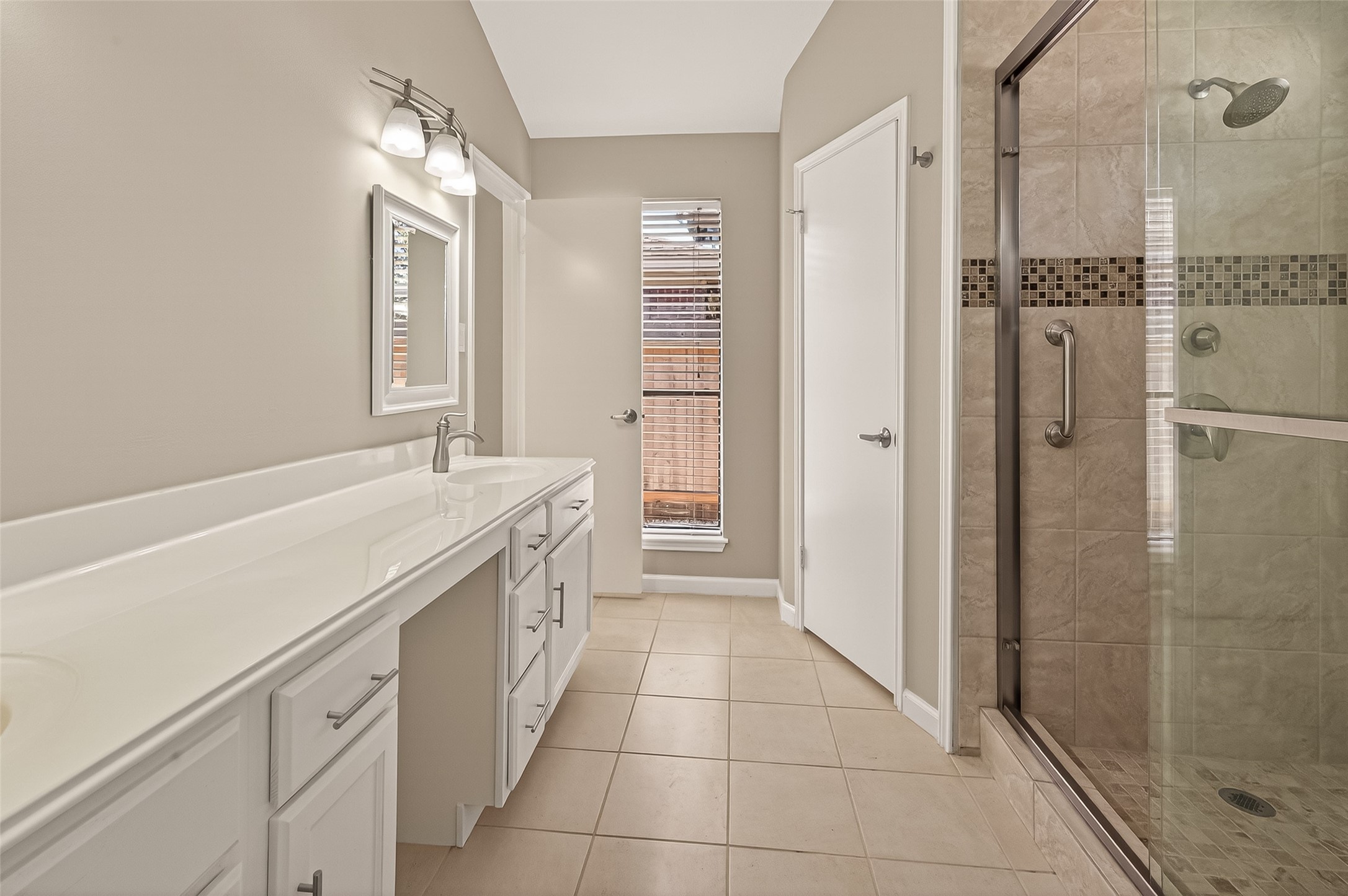 10810 Umber Court Houston, TX 77099 - Photo 31 of 43 This bathroom features a sleek design with a long white double vanity, modern fixtures, and a spacious walk-in glass shower. The neutral tile flooring and soft wall color create a bright and inviting atmosphere.
