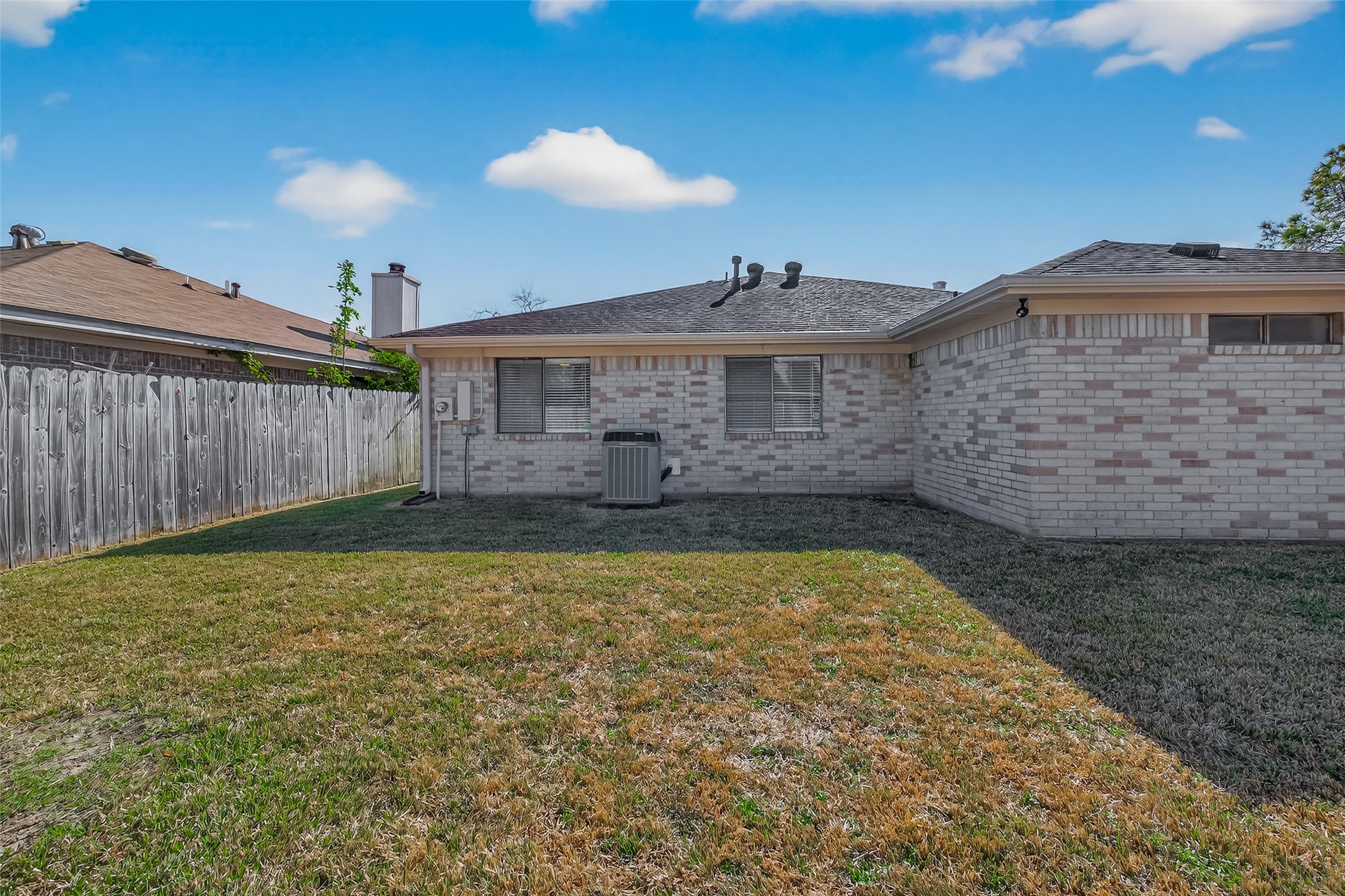 10810 Umber Court Houston, TX 77099 - Photo 41 of 43 This photo shows the backyard of a single-story brick house with a small lawn area. It has a wooden fence on one side and features a central air conditioning unit. The yard offers a manageable space for outdoor activities.