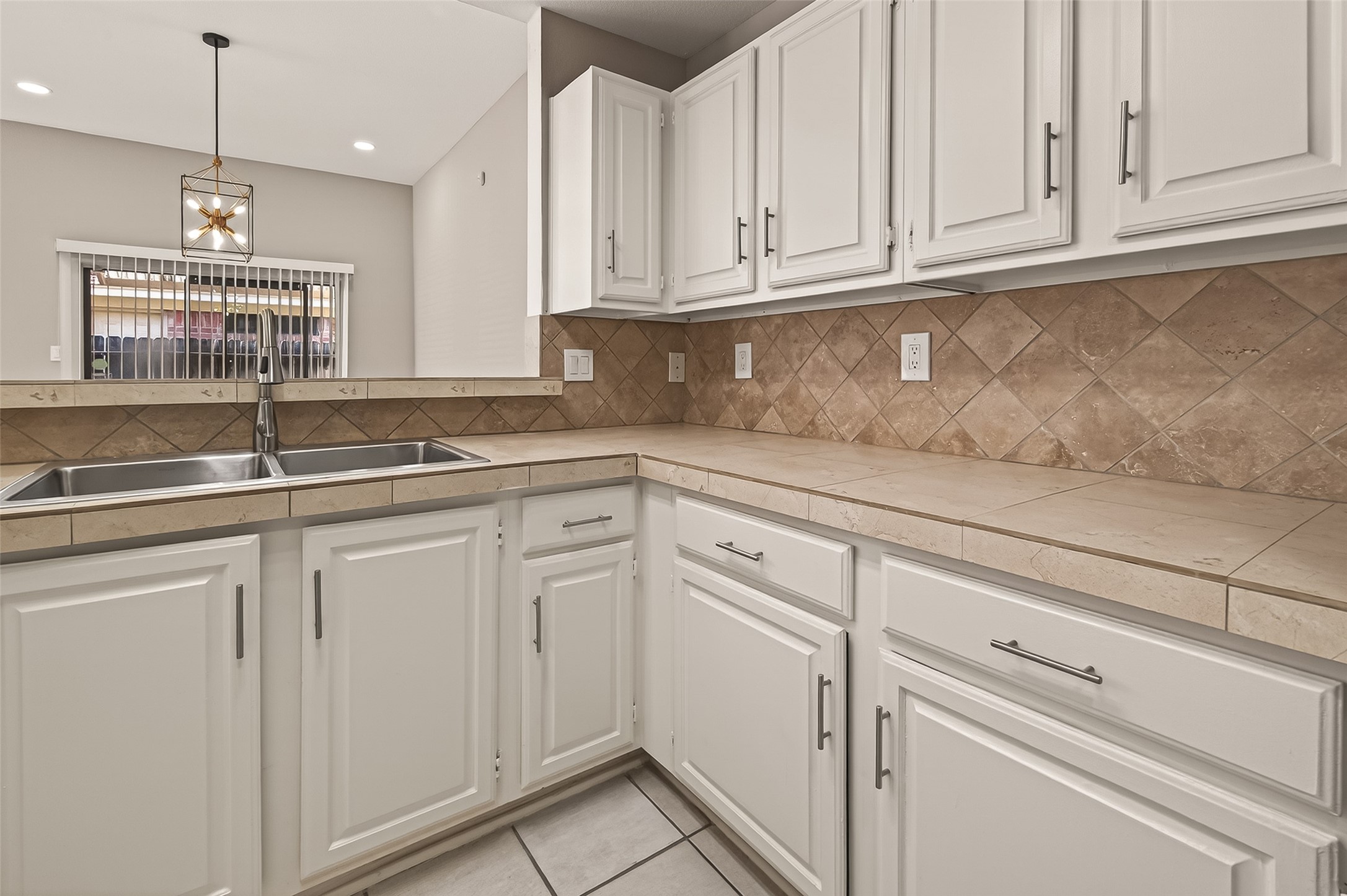 10810 Umber Court Houston, TX 77099 - Photo 10 of 43 A clear view of the kitchen’s functional layout, featuring crisp white cabinetry, durable tile countertops, and a modern gooseneck faucet over a stainless steel double sink.