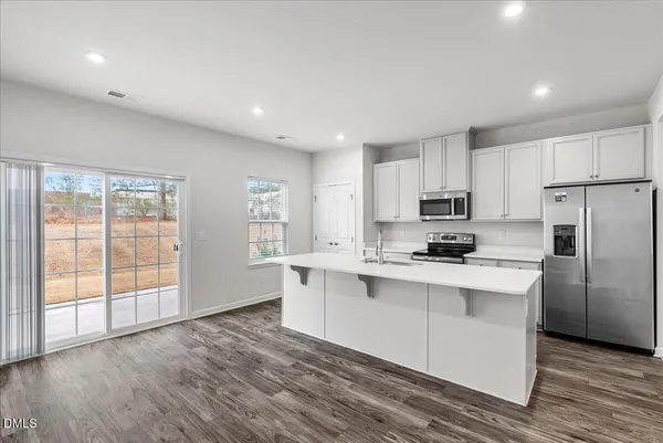 a kitchen with stainless steel appliances granite countertop a stove a sink dishwasher a refrigerator and white cabinets with wooden floor