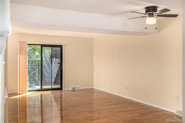 an empty room with wooden floor fan and windows