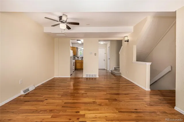a view of an empty room with wooden floor and a ceiling fan