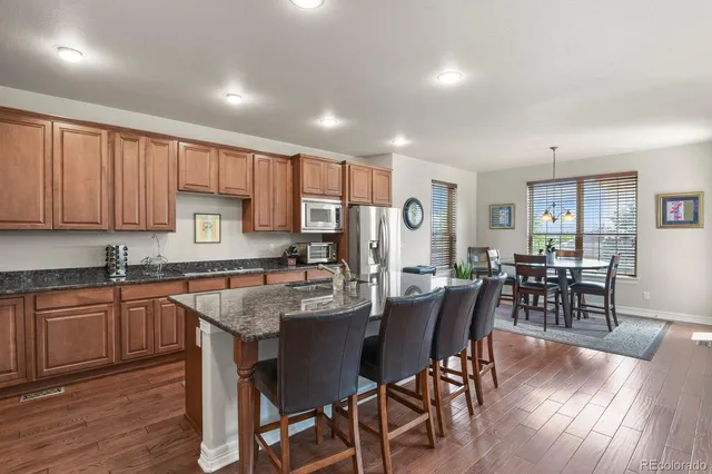 a kitchen with stainless steel appliances granite countertop a stove top oven a sink dishwasher a dining table and chairs with wooden floor