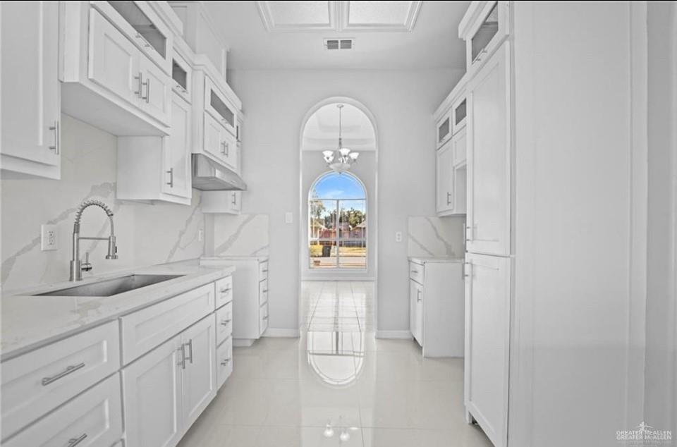 1900 Magnolia Street Mission, TX 78573 - Photo 16 of 25 Kitchen featuring white cabinets, a chandelier, light stone counters, backsplash, and under cabinet range hood