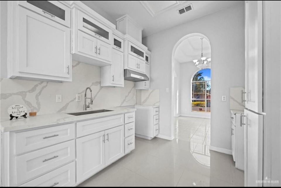 1900 Magnolia Street Mission, TX 78573 - Photo 7 of 25 Kitchen with glass insert cabinets, white cabinets, a chandelier, under cabinet range hood, and light tile patterned flooring