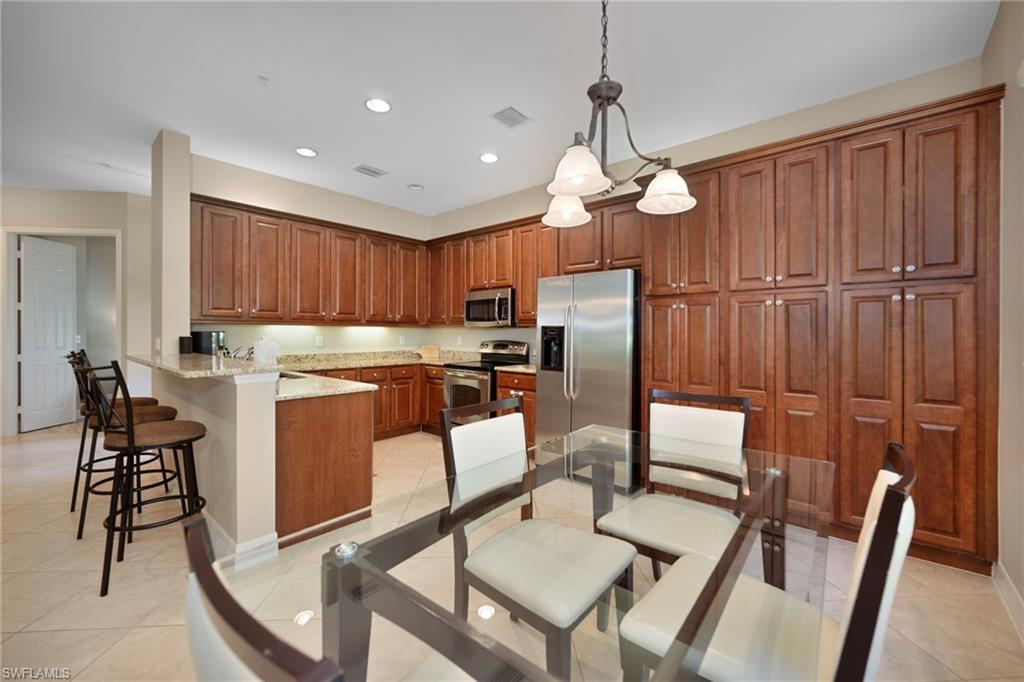 6522 Monterey Point, Unit 101 Naples, FL 34105 - Photo 8 of 29 a kitchen with stainless steel appliances granite countertop a stove a refrigerator a kitchen island a table and chairs with wooden floor